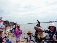 コペンハーゲンの人魚姫を手に乗せて（？）みました。奥にデンマークの国旗、たくさんの観光客も入れると